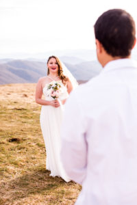 the bride is smiling at the groom as she walks to him on a mountain top