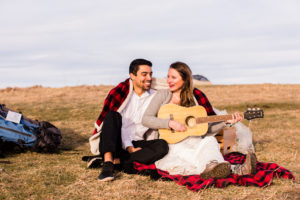 Bride and Groom snuggled up together playing guitar on a mountain top getting ready to camp