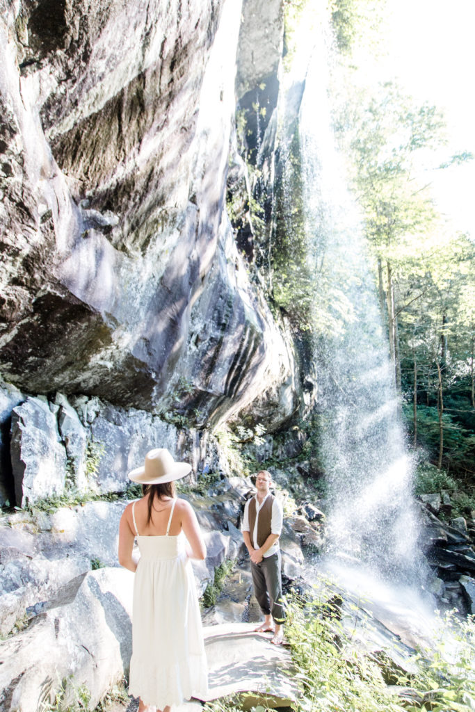 Bride walking towards groom who is at a waterfall during their wedding ceremony